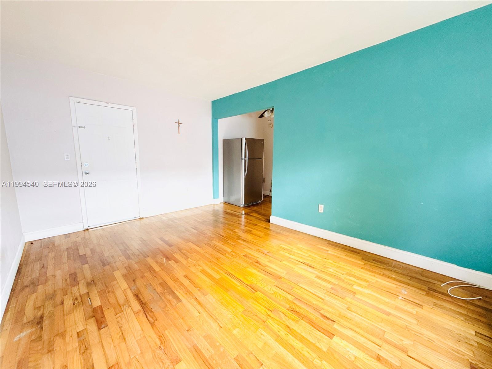 An empty room features hardwood floors, a white door, and a teal accent wall — 555 SW 16th Ave # 11, Miami FL 33135, MIAMI, FL