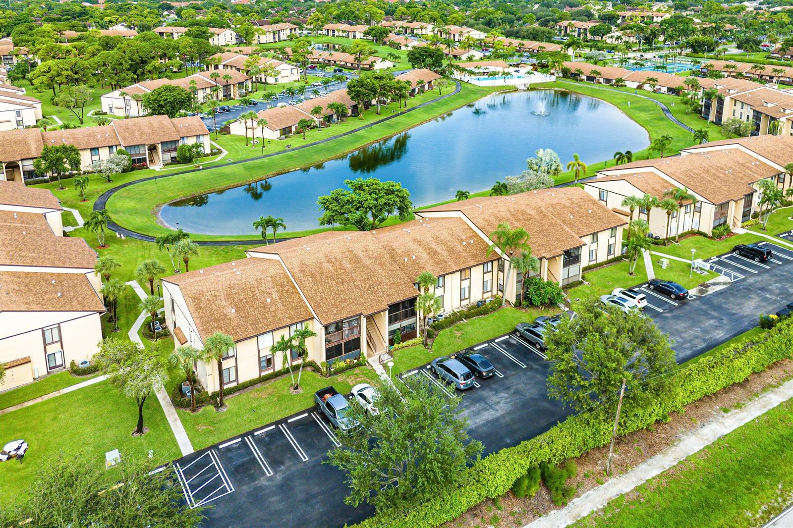 An aerial view shows multi-story apartment buildings surrounding a central pond with parking lots — 826 Sky Pine Way # D1, FL 33415, FL
