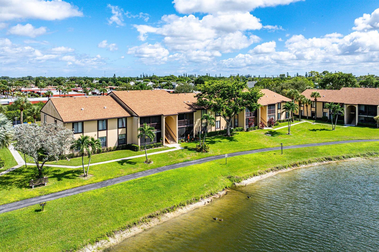 An aerial view shows multi-story apartment buildings situated along a grassy lawn and pond — 826 Sky Pine Way # D1, FL 33415, FL