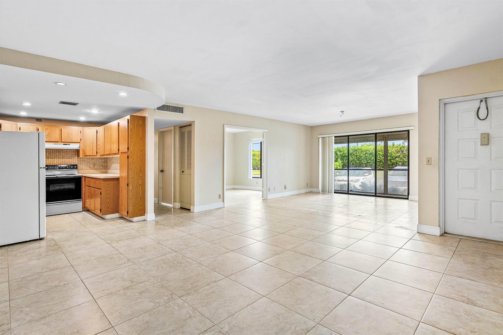 An open-concept living area features light tile flooring, a kitchen with wood cabinets, and sliding doors — 826 Sky Pine Way # D1, FL 33415, FL