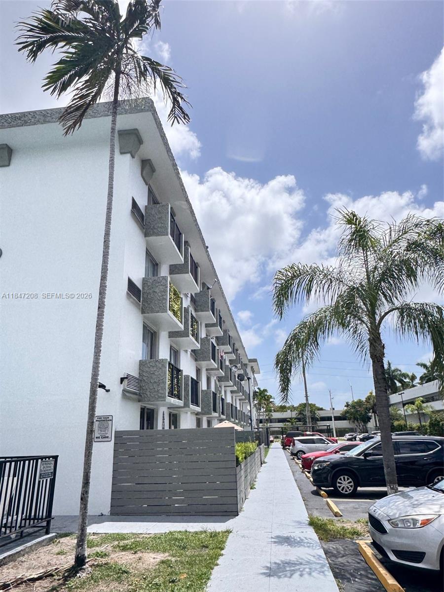 A multi-story white apartment building features balconies and palm trees along a parking lot — 16450 NW 2nd Ave # 207, Miami FL 33169, MIAMI, FL