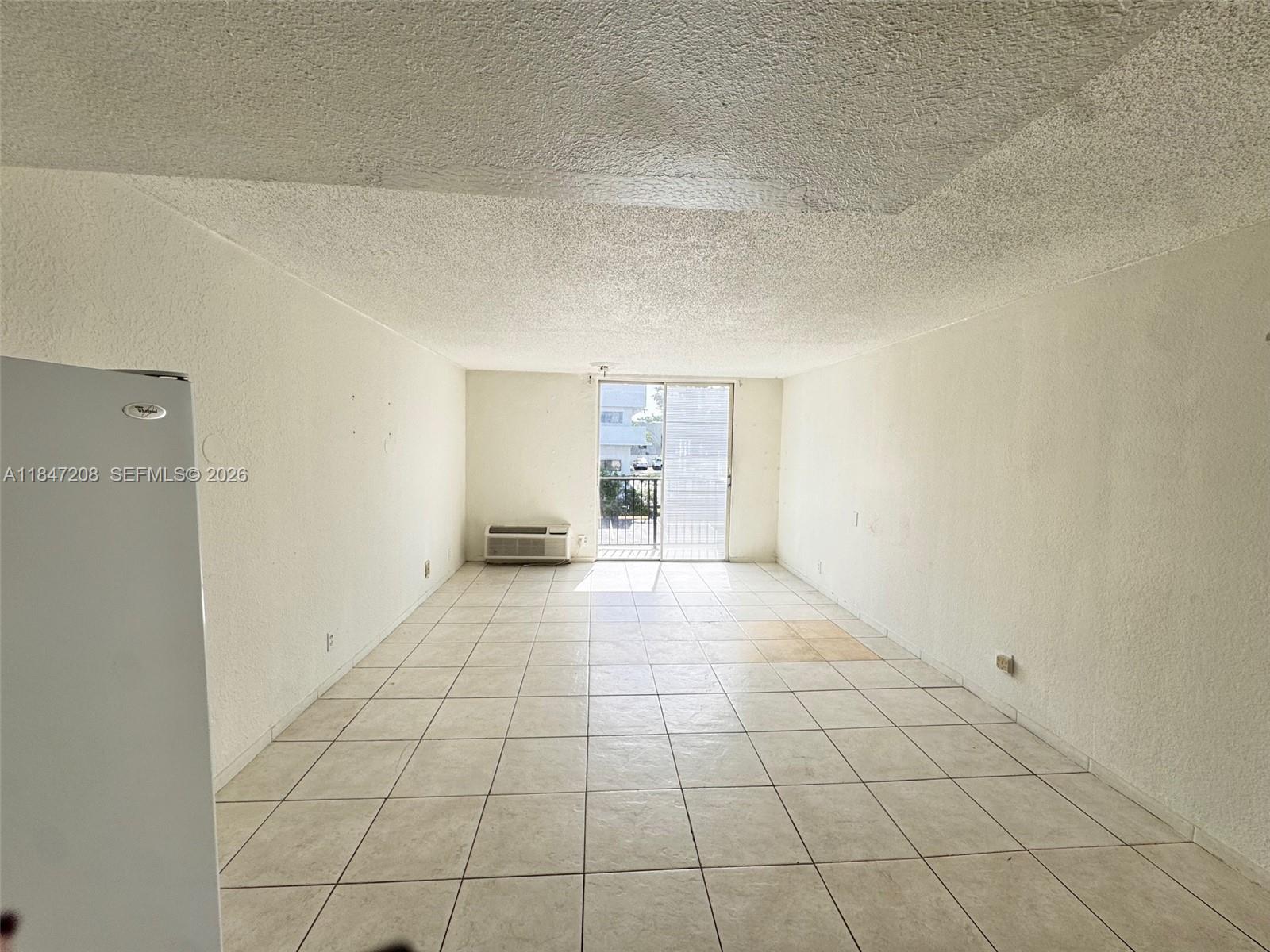 An empty room features white walls, tiled floors, a popcorn ceiling, and a sliding glass door — 16450 NW 2nd Ave # 207, Miami FL 33169, MIAMI, FL