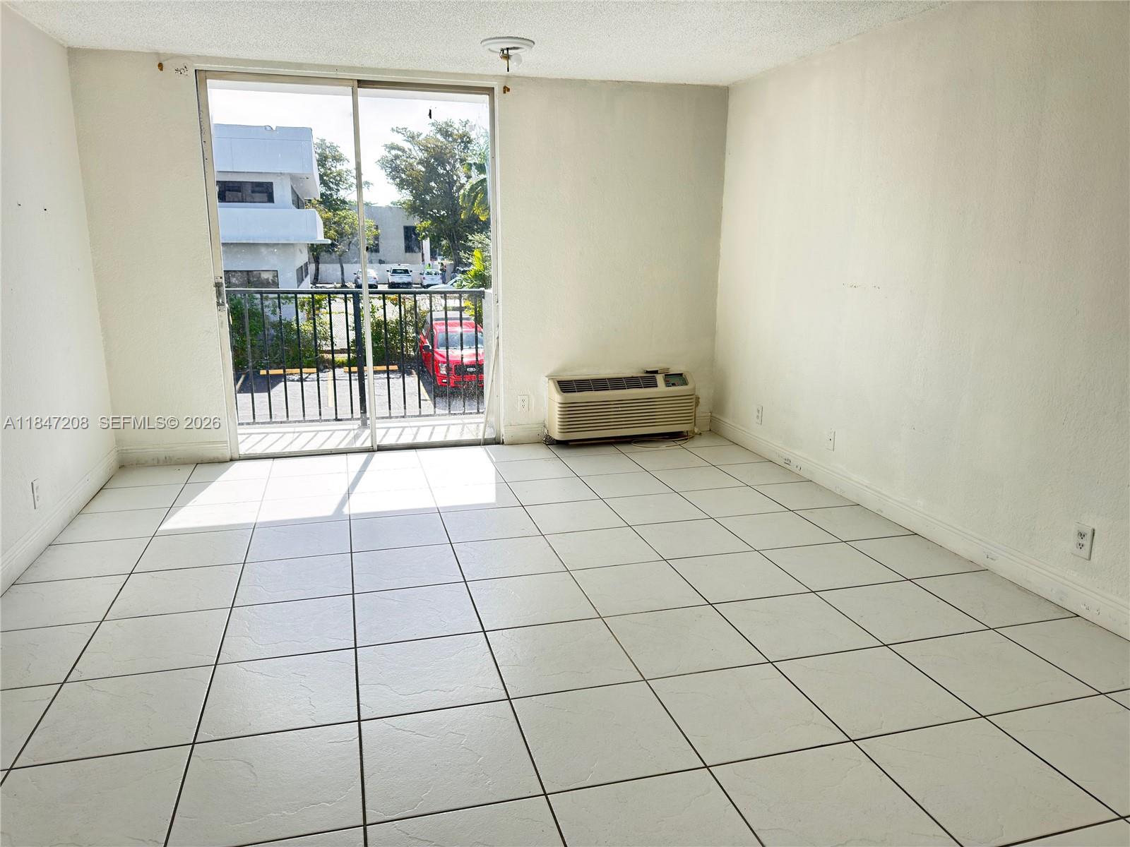 An empty room features white tile flooring, a wall-mounted air conditioner, and a sliding glass door — 16450 NW 2nd Ave # 207, Miami FL 33169, MIAMI, FL
