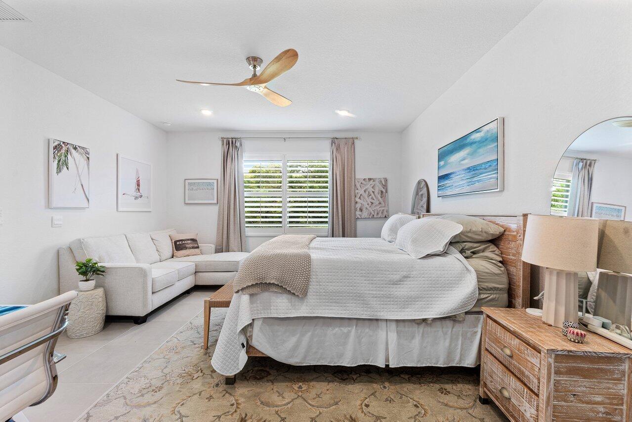 A bedroom features a king bed, a white sectional sofa, and a wooden ceiling fan — 1991 NE Ocean Dunes Drive, Jensen Beach FL 34957, JENSEN BEACH, FL