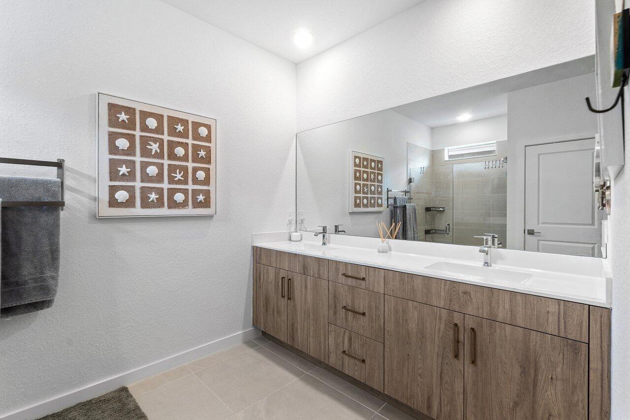 A modern bathroom features a double vanity with wood-grain cabinets and a large wall mirror — 1991 NE Ocean Dunes Drive, Jensen Beach FL 34957, JENSEN BEACH, FL