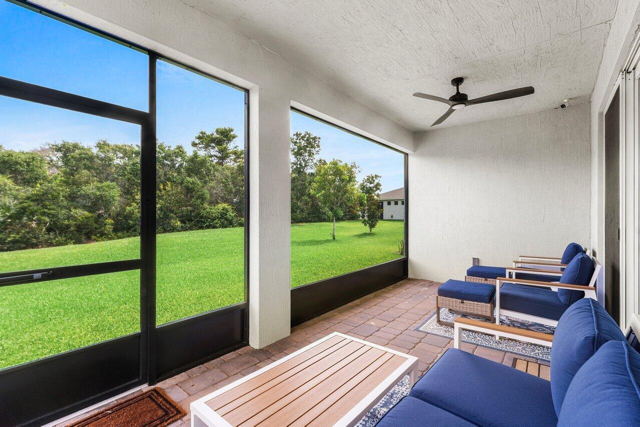 A screened-in patio features a ceiling fan, brick flooring, and outdoor furniture overlooking a lawn — 1991 NE Ocean Dunes Drive, Jensen Beach FL 34957, JENSEN BEACH, FL