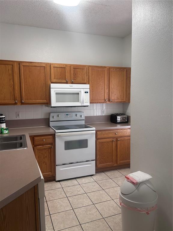 A kitchen features oak cabinets, white appliances, a tiled backsplash, and light-colored floor tiles — 1064 PARK RIDGE CIRCLE, KISSIMMEE, FL