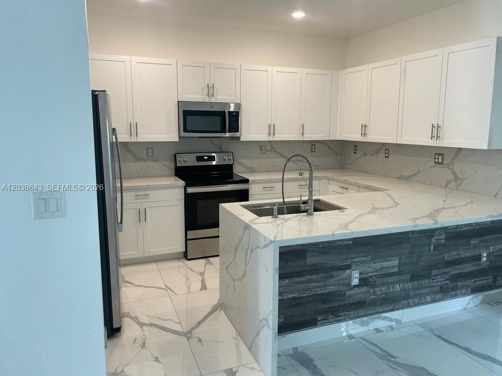 A modern kitchen features white cabinets, stainless steel appliances, and a marble-patterned waterfall island — 10557 W 32nd Ln, Hialeah FL 33018, HIALEAH, FL