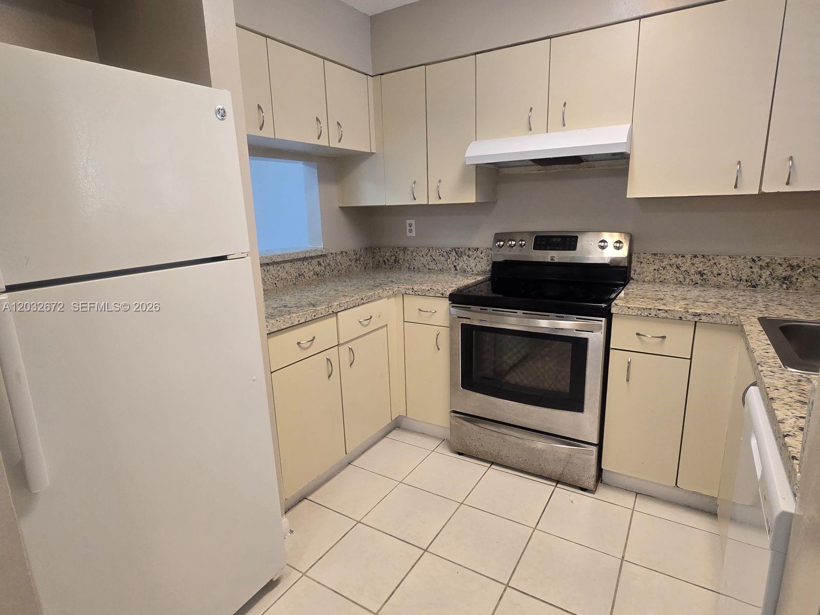 A kitchen features beige cabinets, granite countertops, stainless steel appliances, and white tile flooring — 14961 SW 82nd Ln # 202, Miami FL 33193, MIAMI, FL