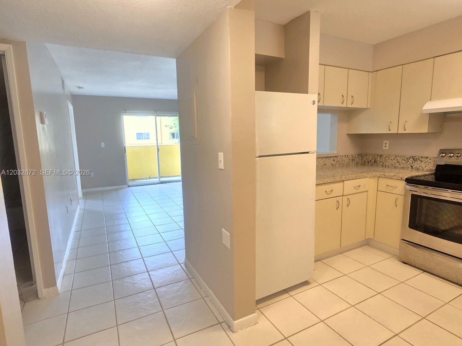 A kitchen with light-colored cabinets and granite countertops opens to a tiled living area — 14961 SW 82nd Ln # 202, Miami FL 33193, MIAMI, FL
