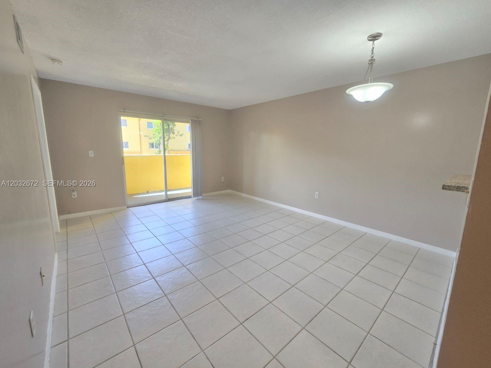 An empty living room features beige walls, white tile flooring, and a sliding glass door — 14961 SW 82nd Ln # 202, Miami FL 33193, MIAMI, FL