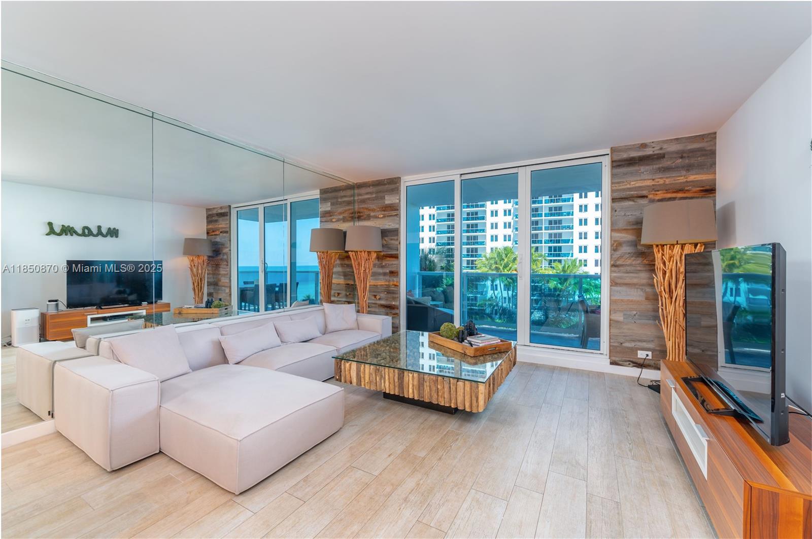 A living room features a light-colored sectional sofa, a glass-topped coffee table, and wood-paneled walls — 2301 Collins Ave # 716, Miami Beach FL 33139, MIAMI BEACH, FL