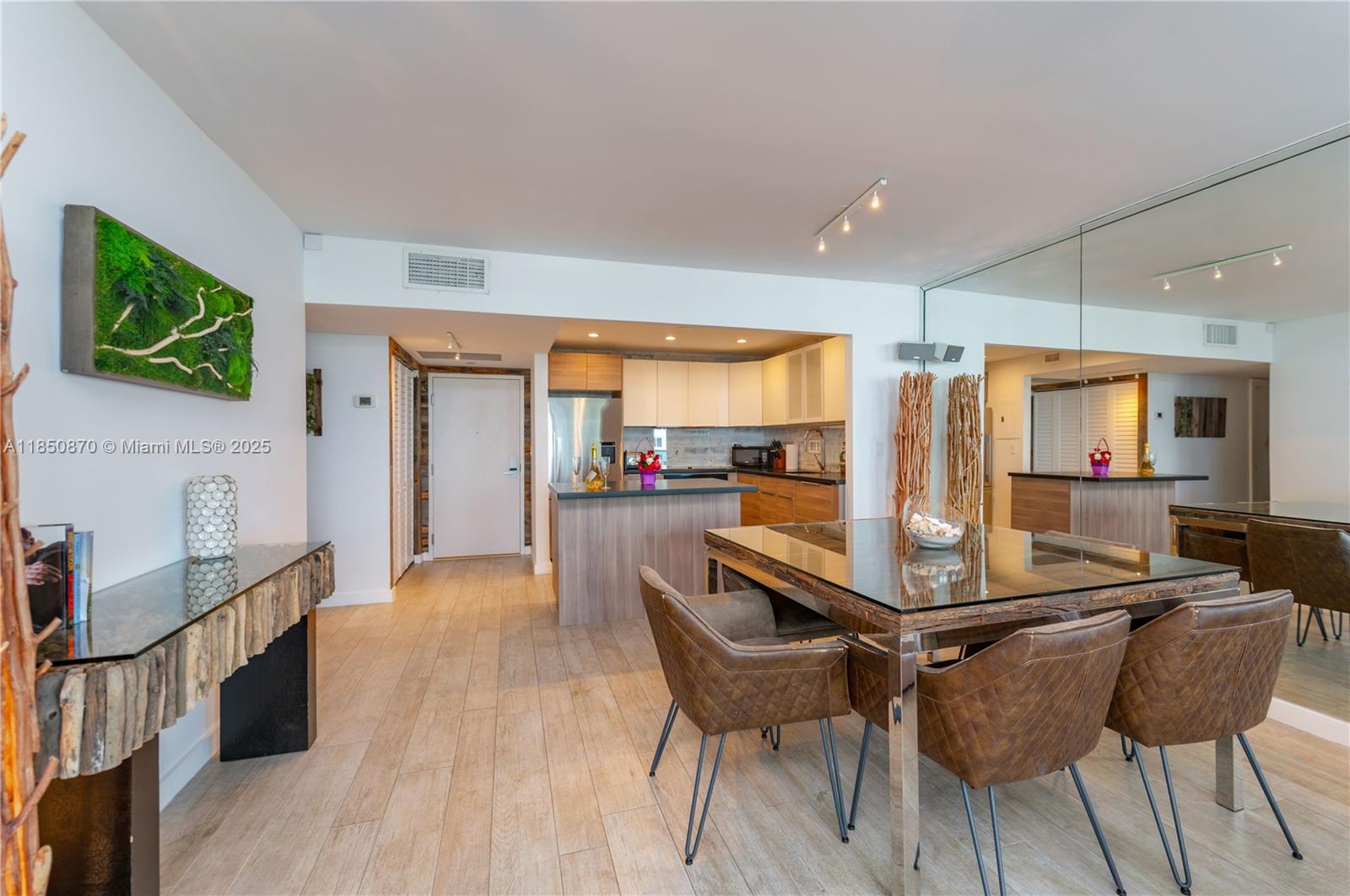 A dining area with a glass table and leather chairs sits adjacent to a modern kitchen — 2301 Collins Ave # 716, Miami Beach FL 33139, MIAMI BEACH, FL