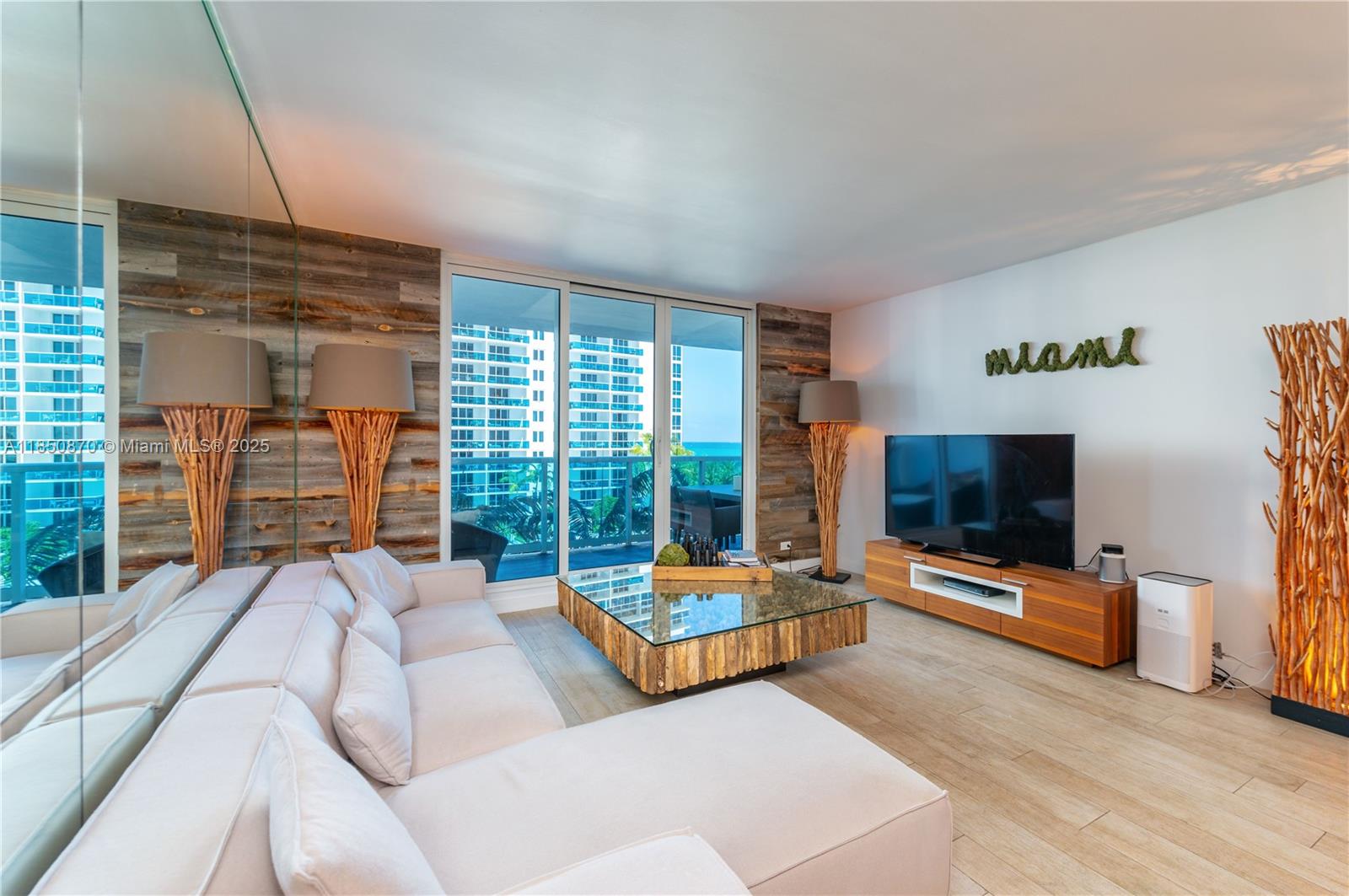A living room features a white sectional sofa, a glass coffee table, and wood-paneled walls — 2301 Collins Ave # 716, Miami Beach FL 33139, MIAMI BEACH, FL