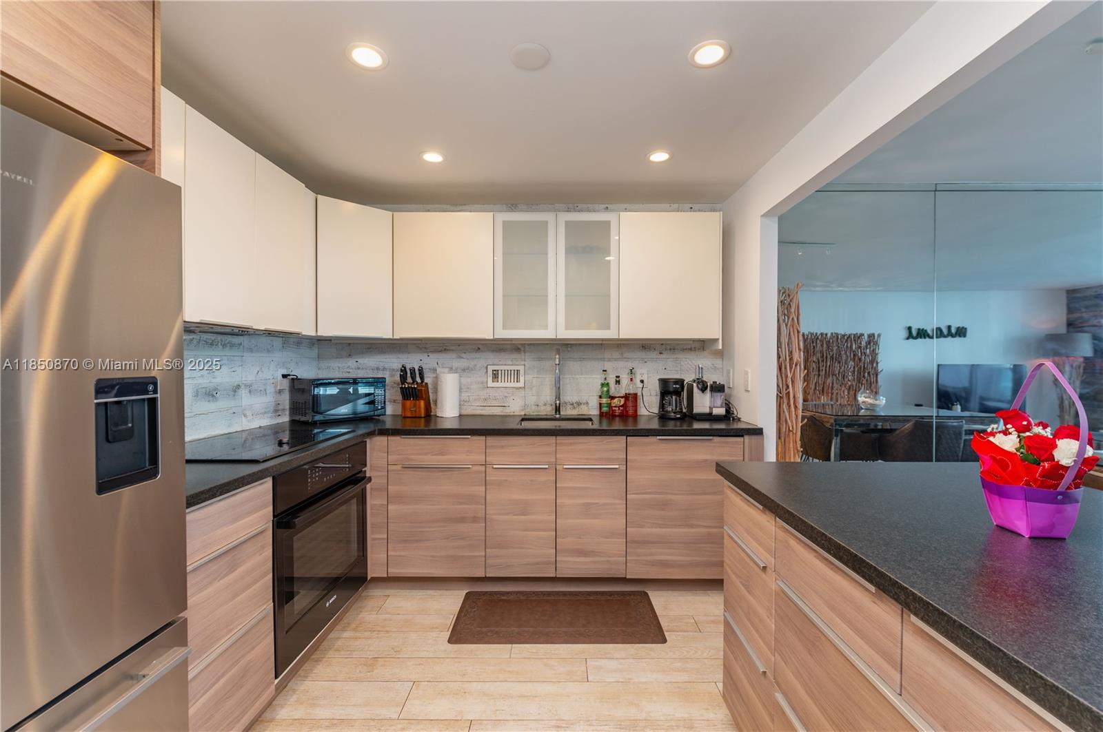 A modern kitchen features light wood cabinetry, white upper cabinets, and dark countertops — 2301 Collins Ave # 716, Miami Beach FL 33139, MIAMI BEACH, FL