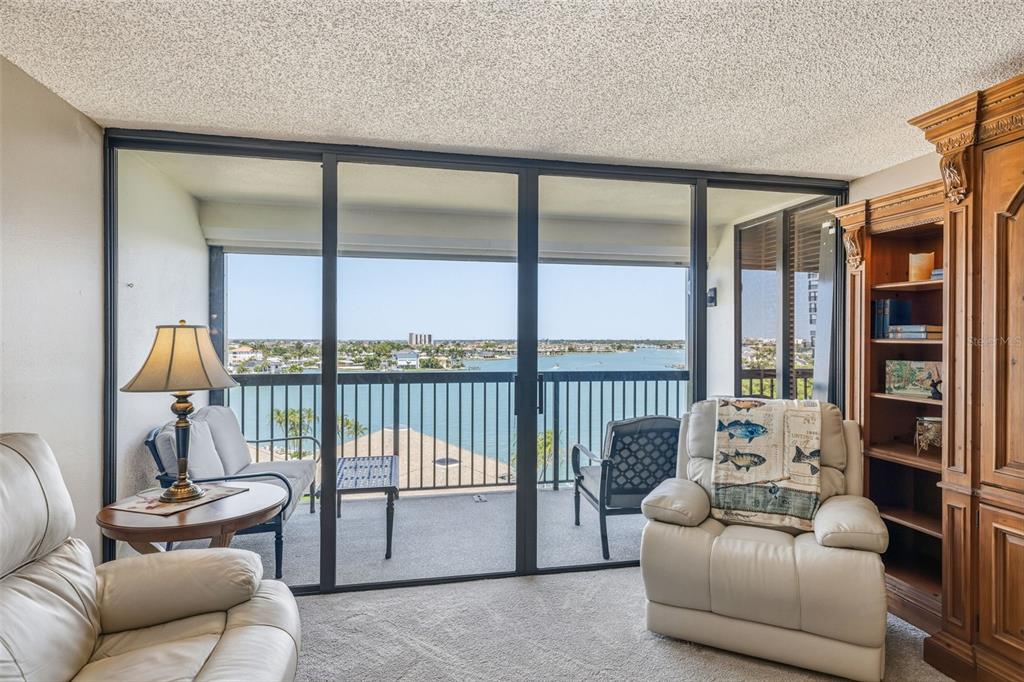 A living room with a beige recliner, a bookshelf, and a balcony overlooking the water — 9425 BLIND PASS ROAD UNIT 705, ST PETE BEACH, FL