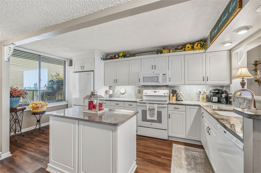 A kitchen with white cabinets, granite countertops, a center island, and a window with blinds — 9425 BLIND PASS ROAD UNIT 705, ST PETE BEACH, FL