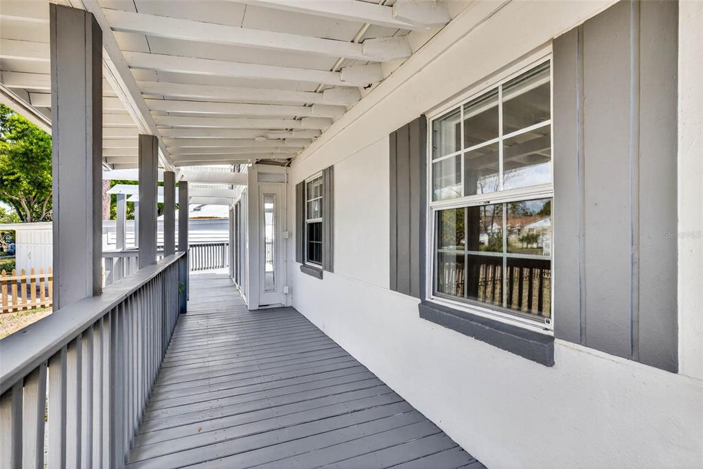 A covered wooden porch with a railing runs alongside a white house with gray shutters — 3620 E TAMPA CIRCLE, TAMPA, FL