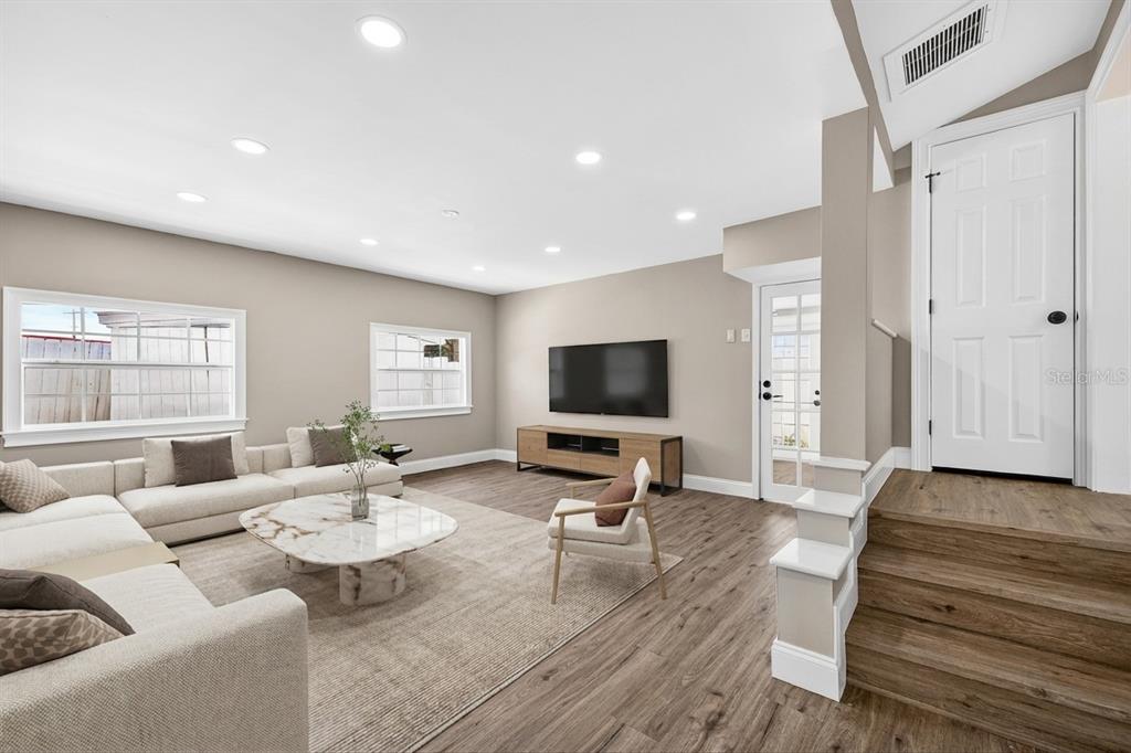 A living room features light wood flooring, a white sectional sofa, and a raised doorway — 3620 E TAMPA CIRCLE, TAMPA, FL
