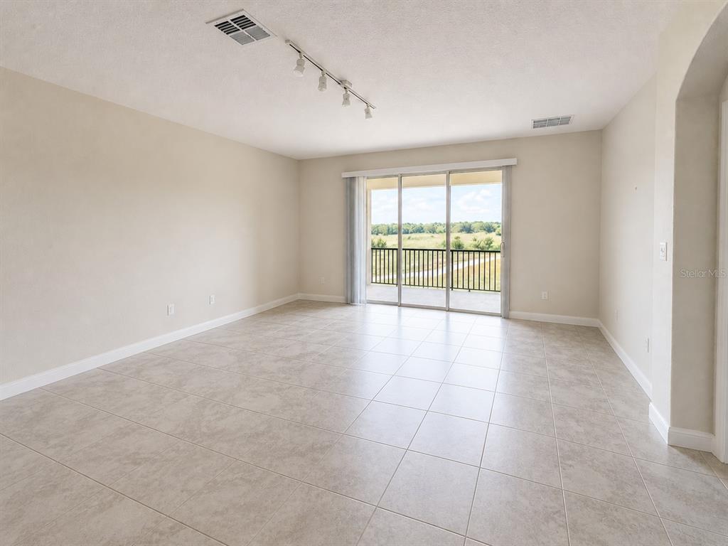 An empty living room with beige walls, tile flooring, track lighting, and a sliding glass door — 505 OCEAN COURSE AVENUE UNIT 505, DAVENPORT, FL