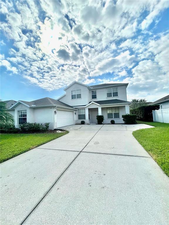 A two-story house with a light-colored exterior, a concrete driveway, and a large cloudy sky — 2370 HINSDALE DRIVE, KISSIMMEE, FL