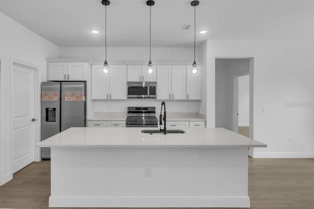 A modern kitchen features a large white island, stainless steel appliances, and white cabinetry — 16954 SW 39TH CIRCLE, OCALA, FL