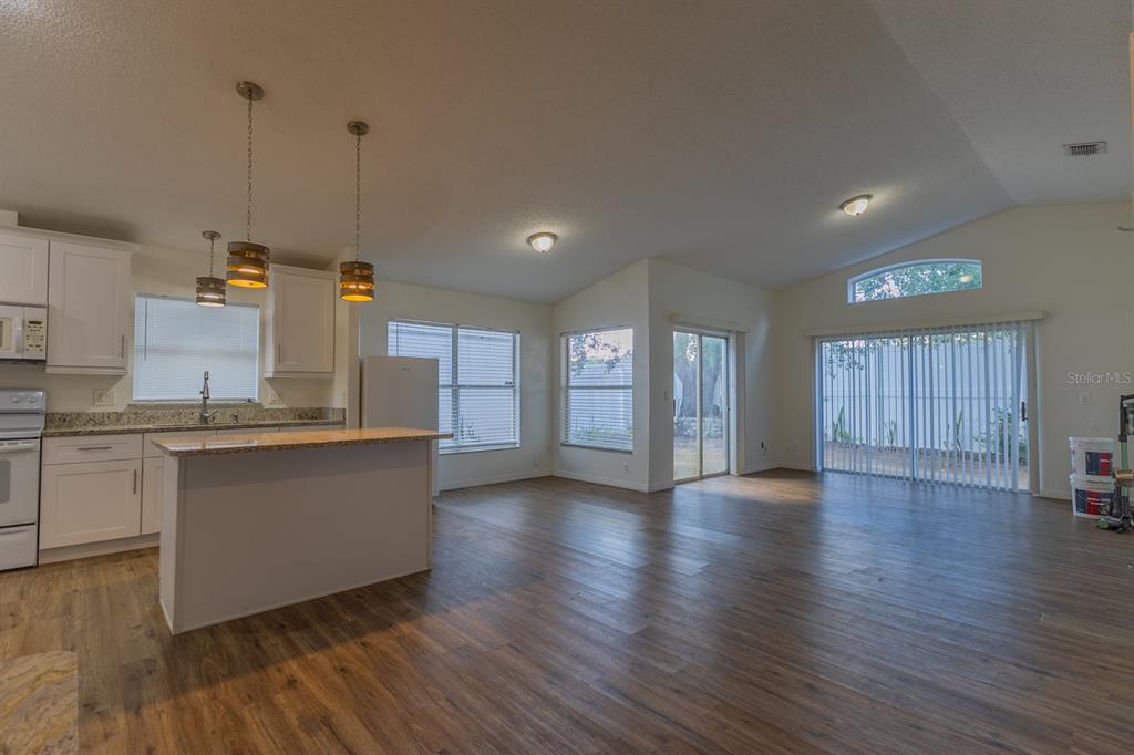 An open-concept kitchen and living area with wood-look flooring, white cabinets, and sliding glass doors — 3267 BREWSTER DRIVE, KISSIMMEE, FL