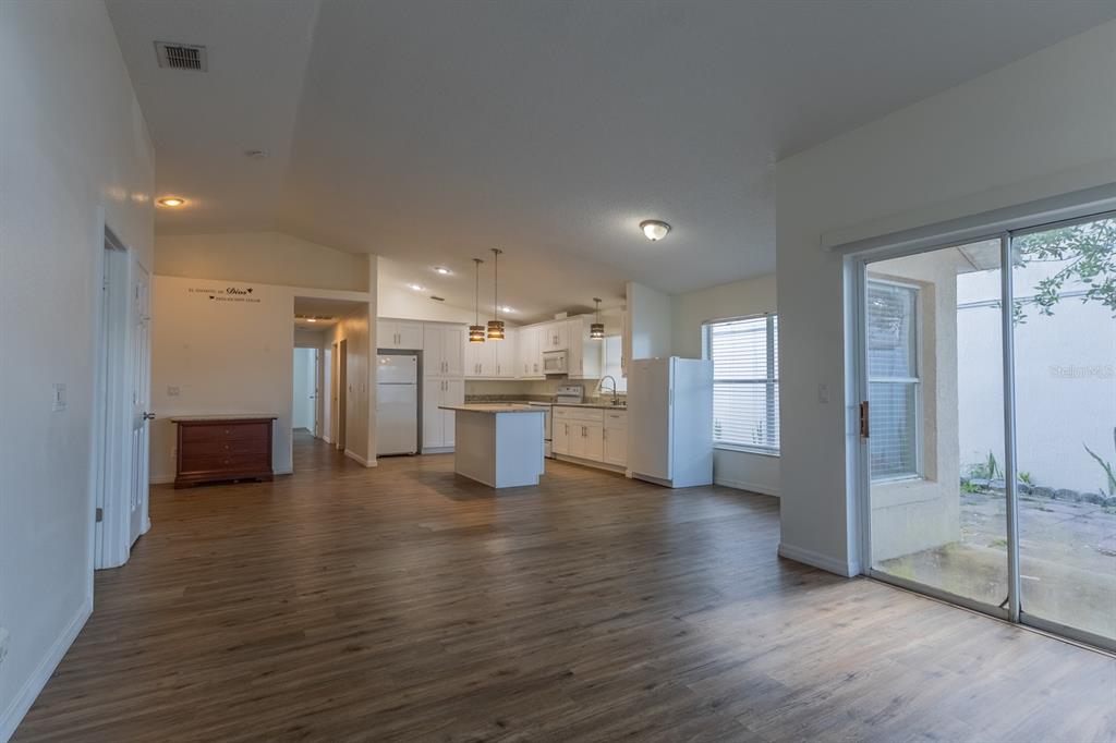 An open-concept kitchen and living area feature white cabinetry, a center island, and wood flooring — 3267 BREWSTER DRIVE, KISSIMMEE, FL