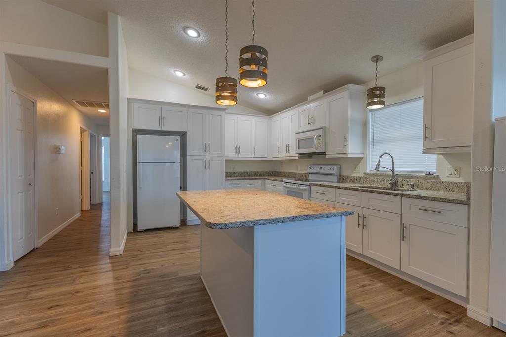 A kitchen with white cabinets, granite countertops, a central island, and wood-look flooring — 3267 BREWSTER DRIVE, KISSIMMEE, FL