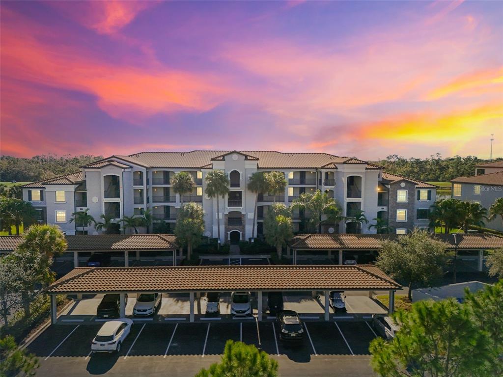 An aerial view of a multi-story apartment building with covered parking spaces in the foreground — 16904 VARDON TERRACE UNIT 107, BRADENTON, FL