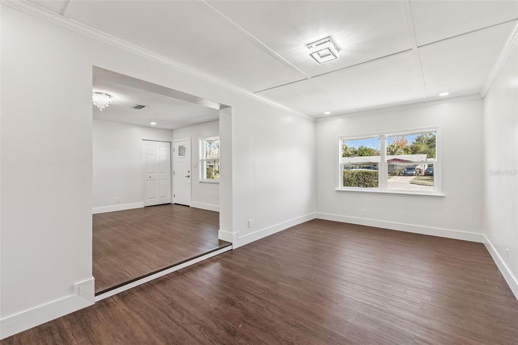 An interior view shows a white-walled living area with dark wood-look flooring and a window — 1070 N LIBBY COURT, DAYTONA BEACH, FL
