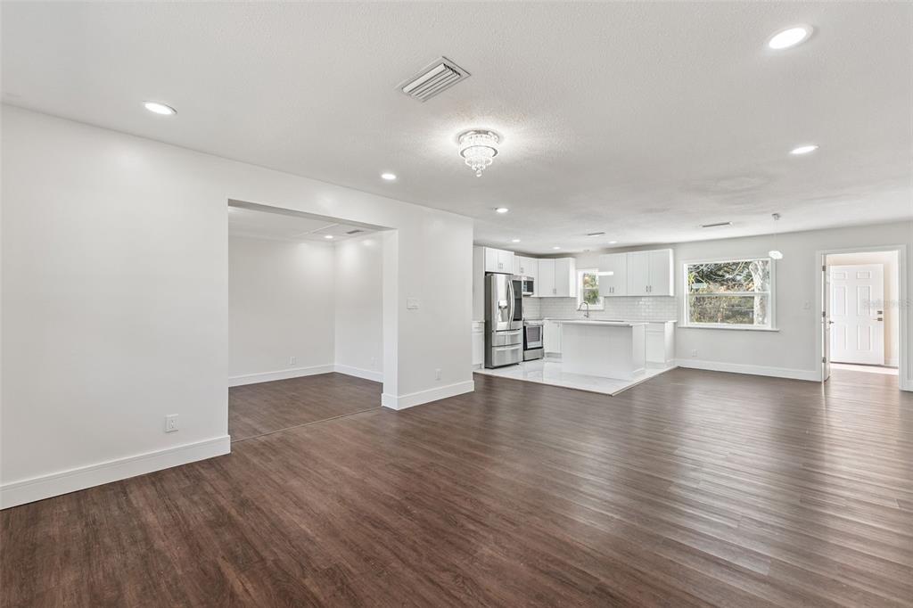 A bright, open-concept living area with dark wood-look flooring and a white kitchen in back — 1070 N LIBBY COURT, DAYTONA BEACH, FL