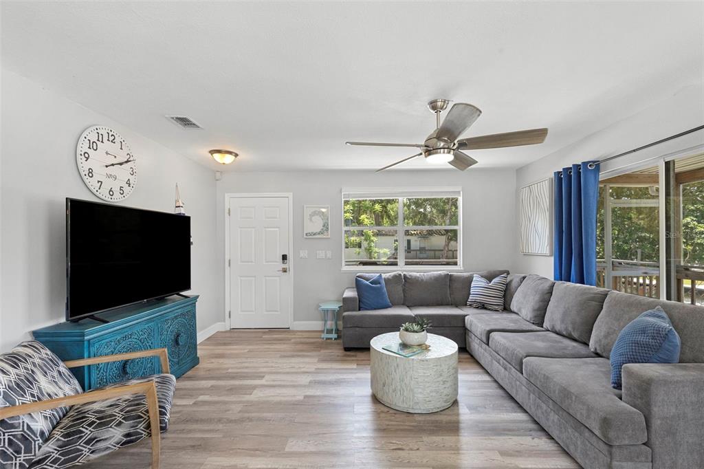 A living room features a grey sectional sofa, a blue media console, and wood-look flooring — 6183 WAVERLY ROAD, WEEKI WACHEE, FL