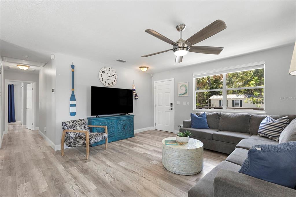 A living room features a grey sectional sofa, a blue media console, and wood-look flooring — 6183 WAVERLY ROAD, WEEKI WACHEE, FL