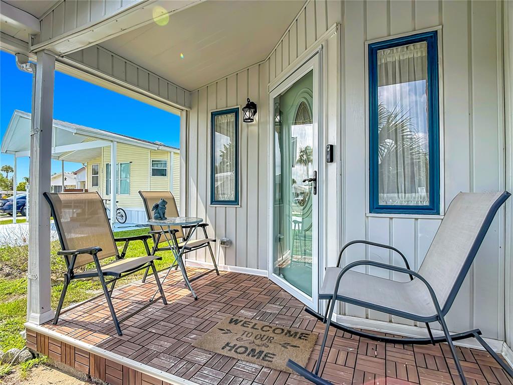 A covered porch features a tiled floor, two chairs, a small table, and a front door — 9000 US HWY 192 UNIT 297, CLERMONT, FL