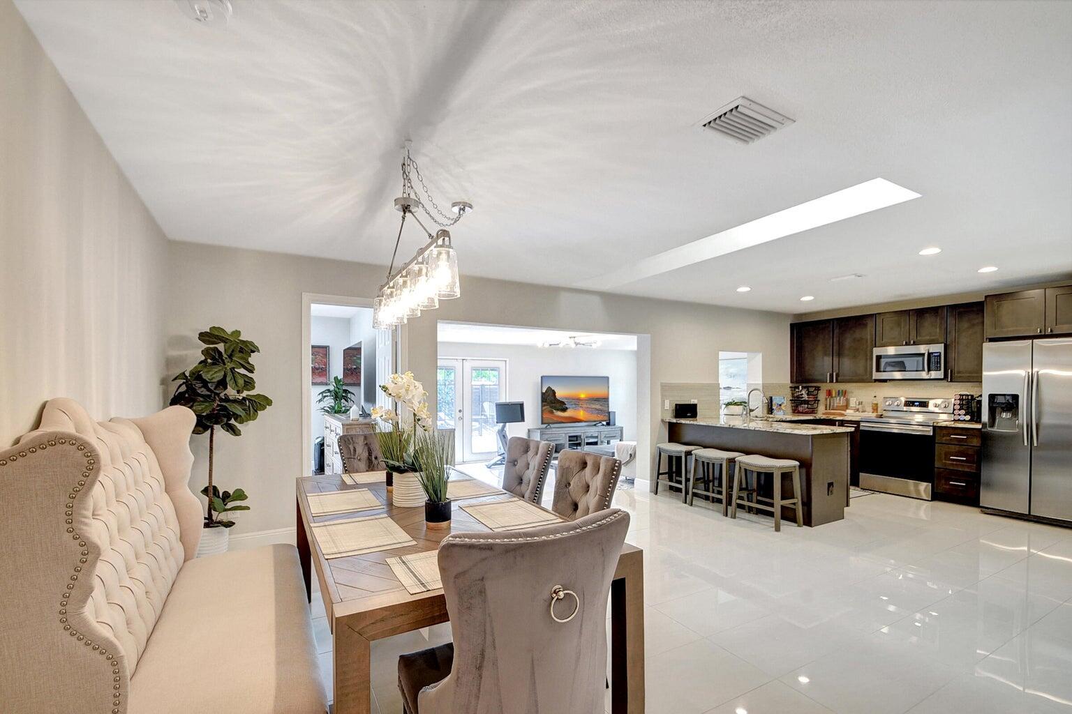 An open-concept dining area and kitchen featuring tiled floors, dark cabinetry, and a light fixture — 702 Grove Street, FL 33461, FL