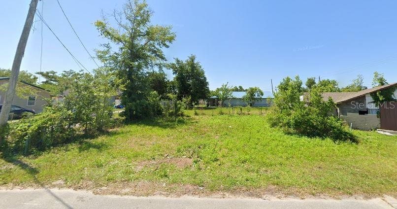 A vacant, grassy residential lot sits between two existing houses under a clear blue sky — 2702 E 9TH STREET, PANAMA CITY, FL