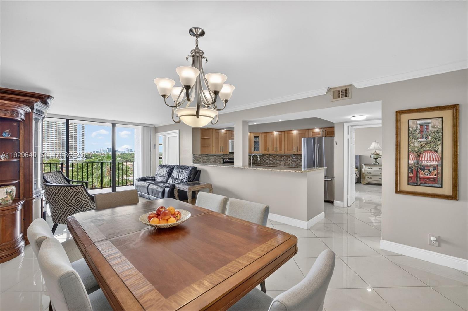 A dining area with a wooden table and chandelier opens to a kitchen and balcony — 200 Leslie Dr # 707, Hallandale Beach FL 33009, HALLANDALE BEACH, FL