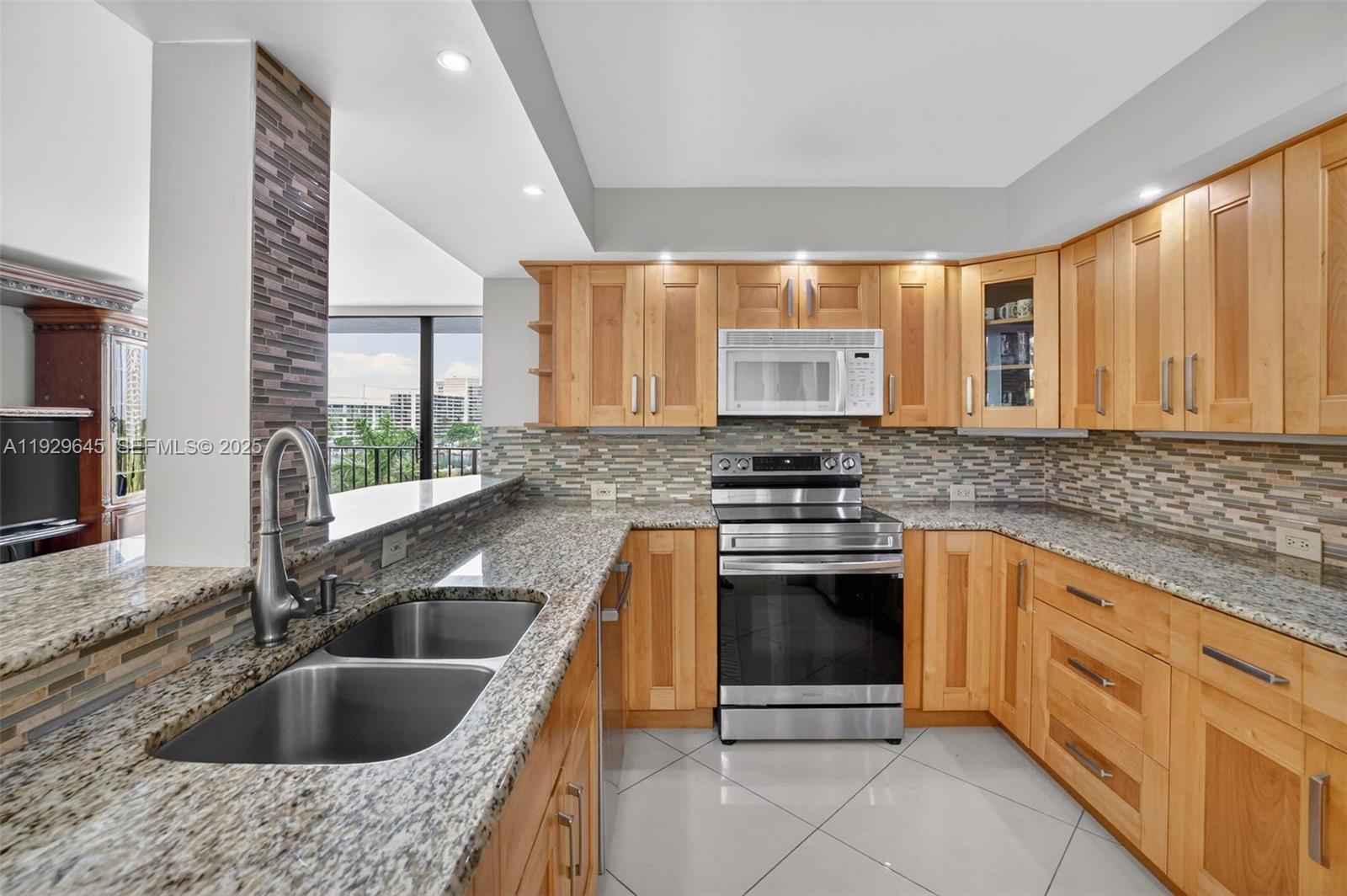 A kitchen features light wood cabinets, granite countertops, stainless steel appliances, and a tile backsplash — 200 Leslie Dr # 707, Hallandale Beach FL 33009, HALLANDALE BEACH, FL