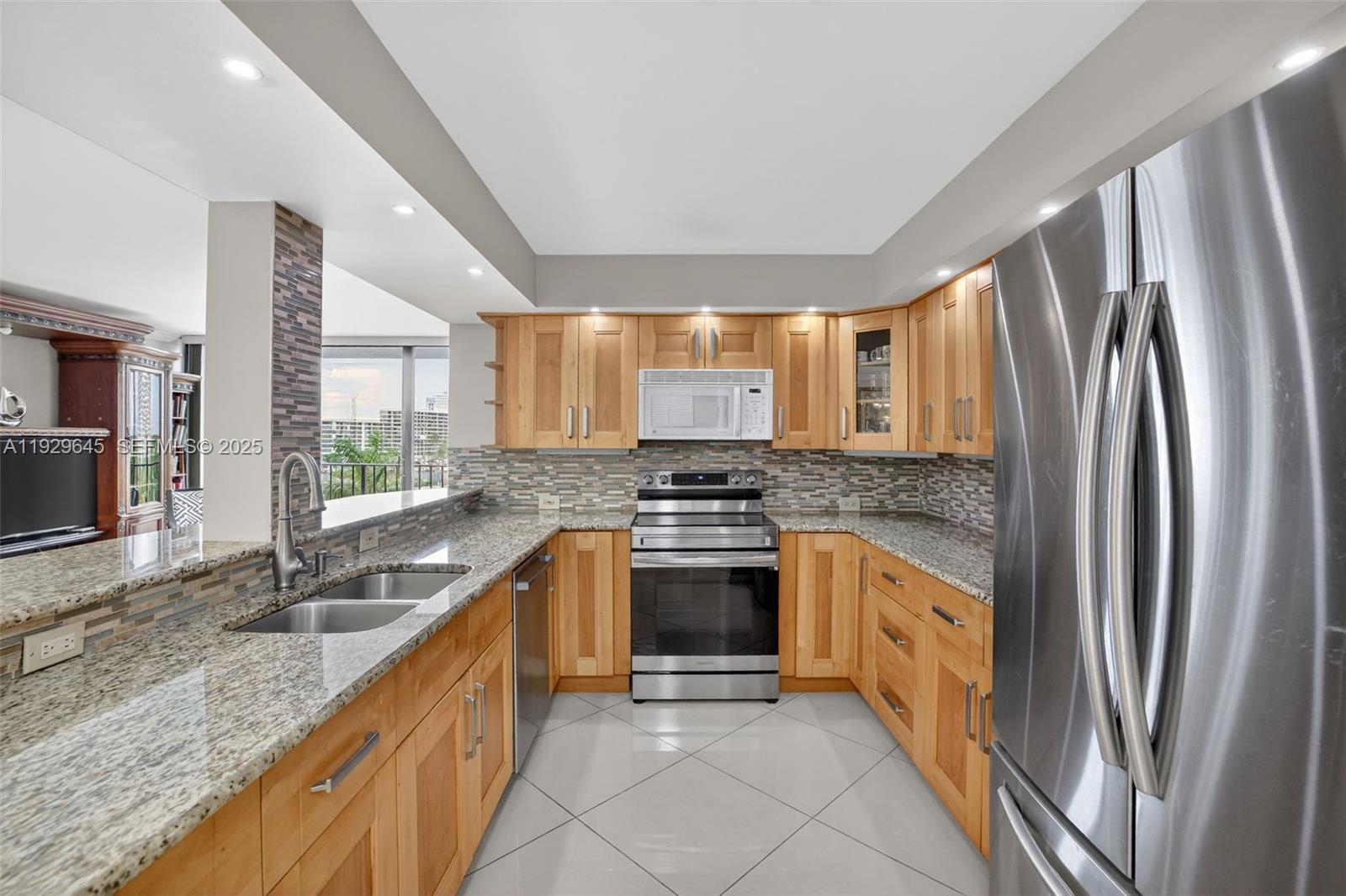 A kitchen features light wood cabinets, granite countertops, stainless steel appliances, and a tile backsplash — 200 Leslie Dr # 707, Hallandale Beach FL 33009, HALLANDALE BEACH, FL