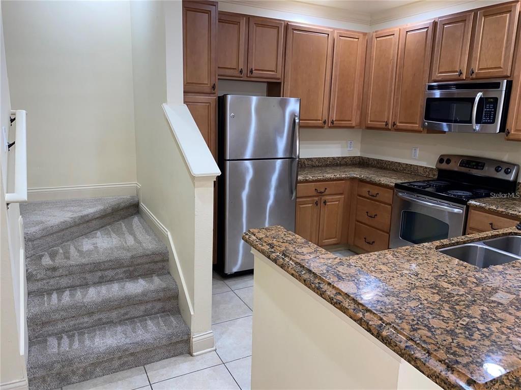 A kitchen with wood cabinets, granite countertops, stainless steel appliances, and adjacent carpeted stairs — 3008 BELLA VISTA DRIVE, DAVENPORT, FL