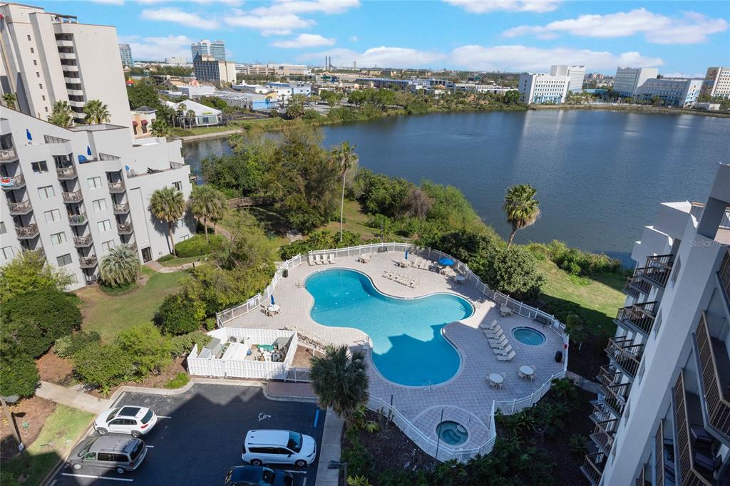 An aerial view shows a swimming pool and hot tub next to a lake — 6165 CARRIER DRIVE UNIT 2201, ORLANDO, FL