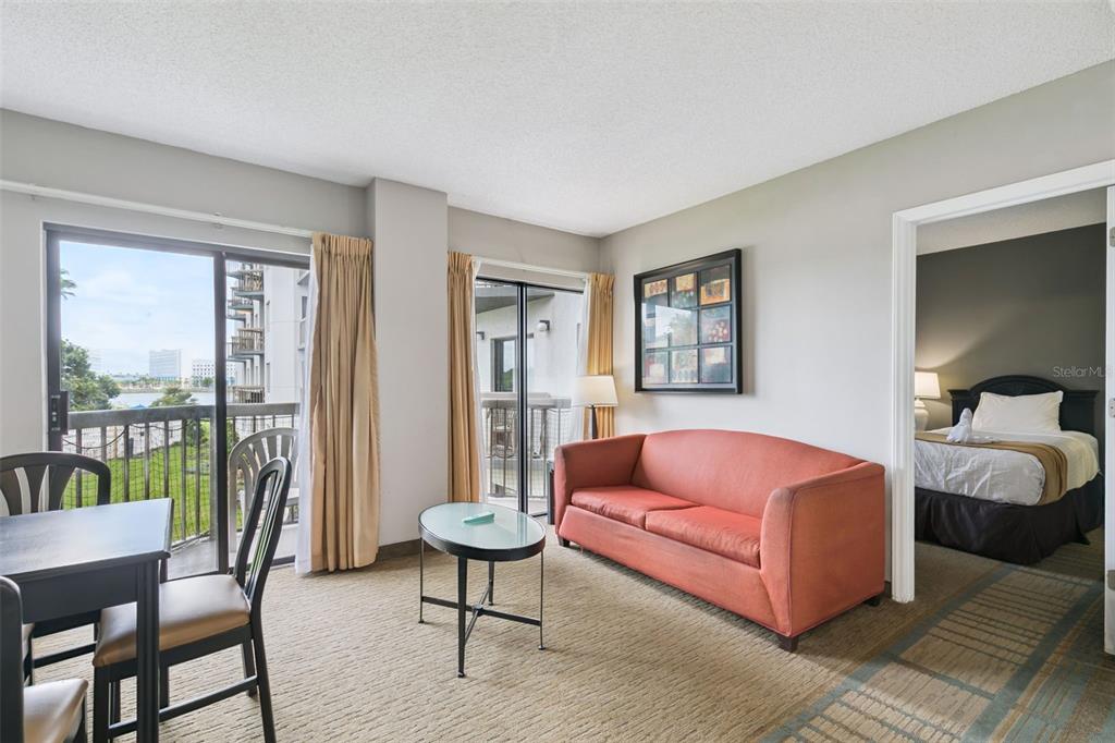 A living room with a red sofa, glass coffee table, and an adjacent bedroom — 6165 CARRIER DRIVE UNIT 2201, ORLANDO, FL