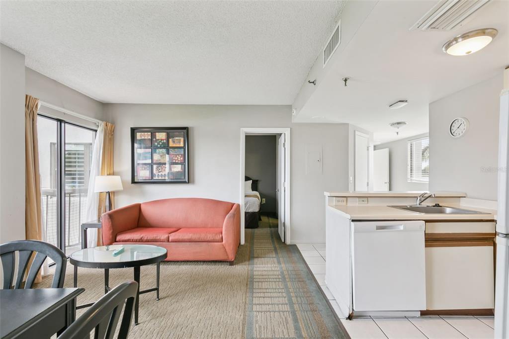 A living room with a coral sofa, a small dining area, and an adjacent kitchen — 6165 CARRIER DRIVE UNIT 2201, ORLANDO, FL