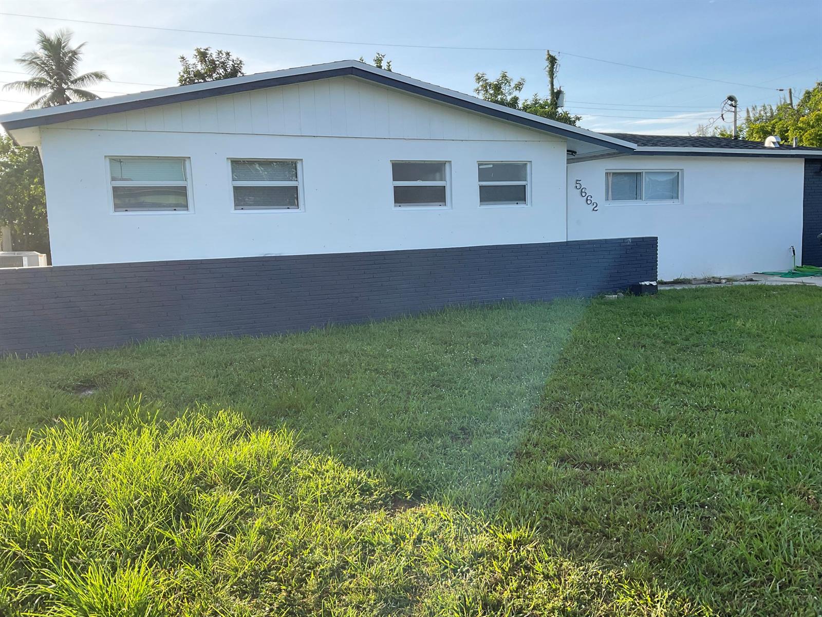 A single-story house with white siding and a dark gray brick base under a blue sky — 5662 Parke Avenue, West Palm Beach FL 33407, WEST PALM BEACH, FL