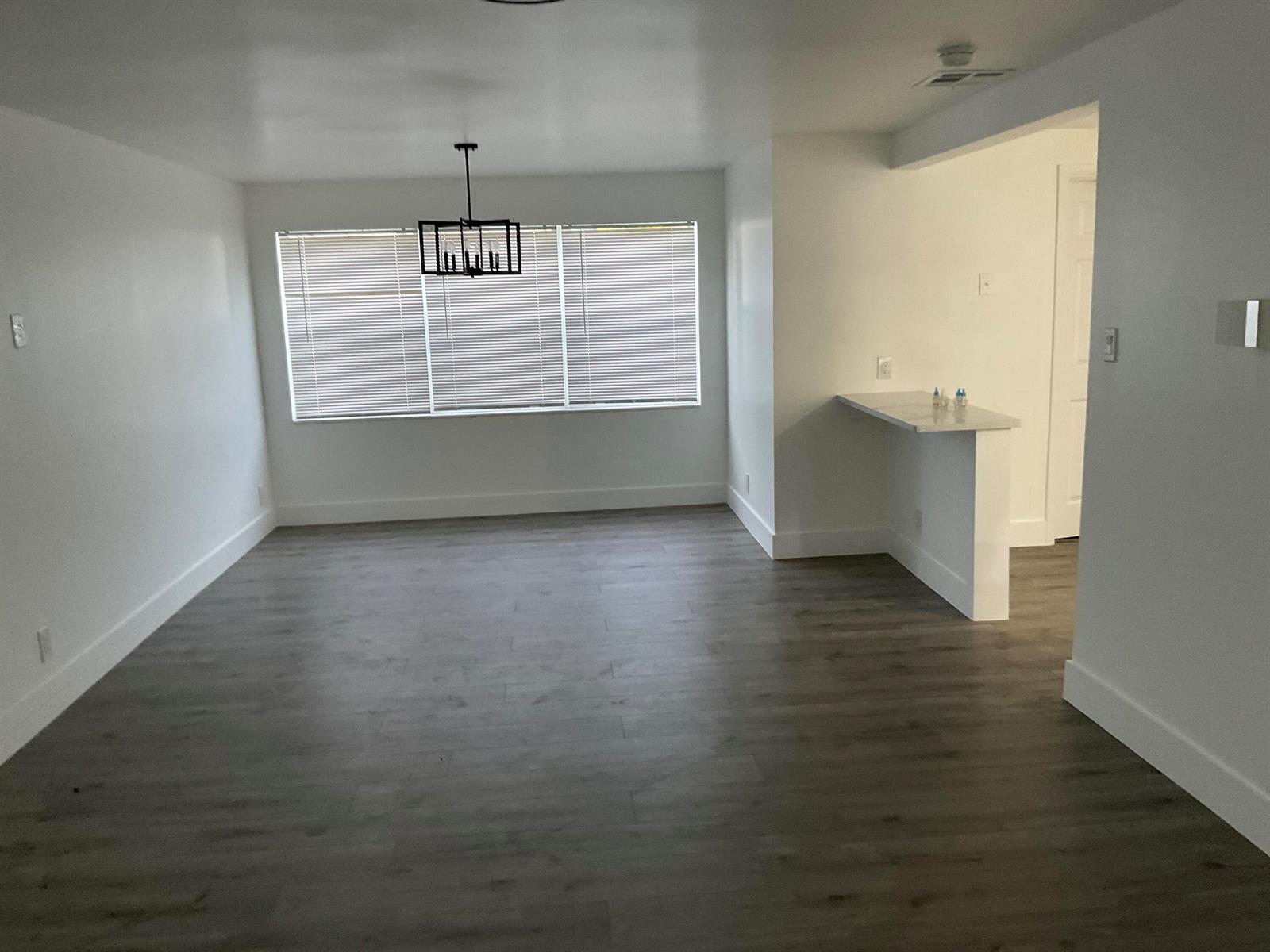 An empty room features white walls, gray wood-look flooring, a chandelier, and a breakfast bar — 5662 Parke Avenue, West Palm Beach FL 33407, WEST PALM BEACH, FL