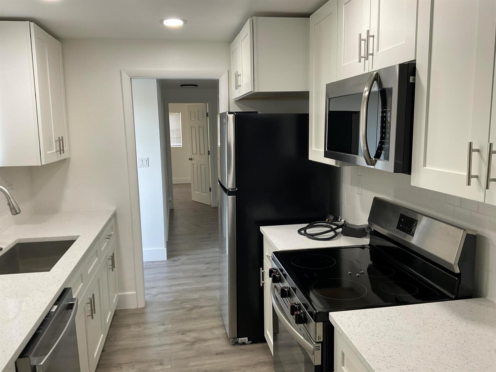 A kitchen features white cabinets, stainless steel appliances, and light-colored countertops — 5662 Parke Avenue, West Palm Beach FL 33407, WEST PALM BEACH, FL