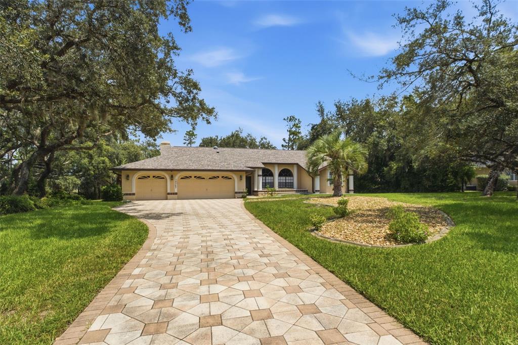 A single-story house with a paved driveway, a three-car garage, and mature trees in front — 10307 WATERS EDGE COURT, WEEKI WACHEE, FL