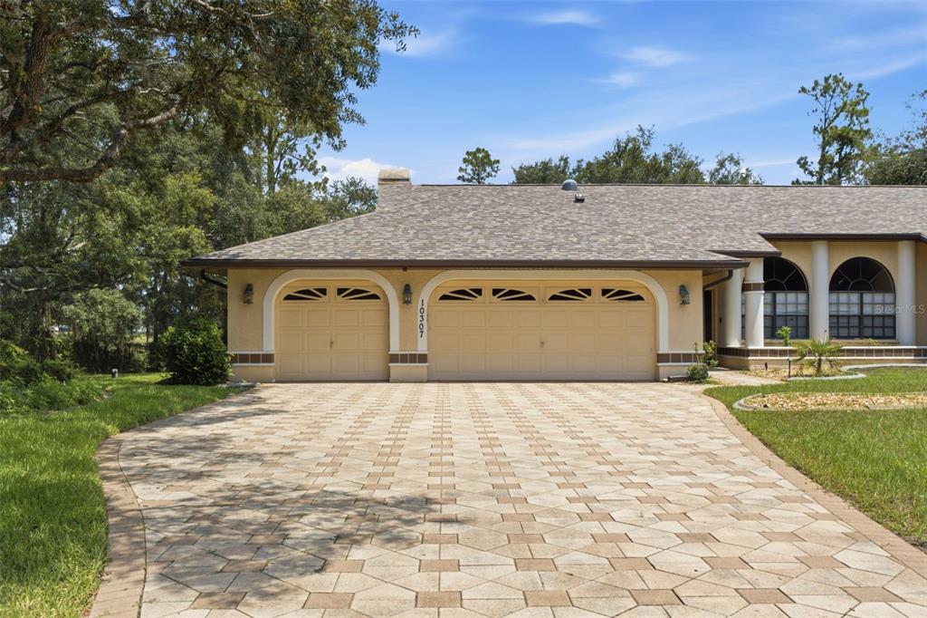 A beige house exterior features a three-car garage and a large paved driveway — 10307 WATERS EDGE COURT, WEEKI WACHEE, FL