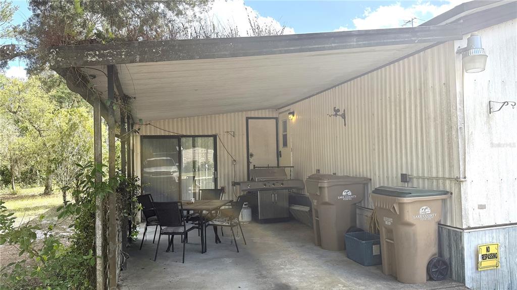A covered patio area features a dining set, a grill, and two large trash bins — 28520 HOLLY AVENUE, PAISLEY, FL